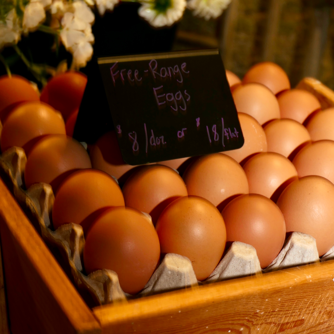 Farm fresh brown free range eggs displayed in a wooden crate with a chalkboard price sign at the community market.