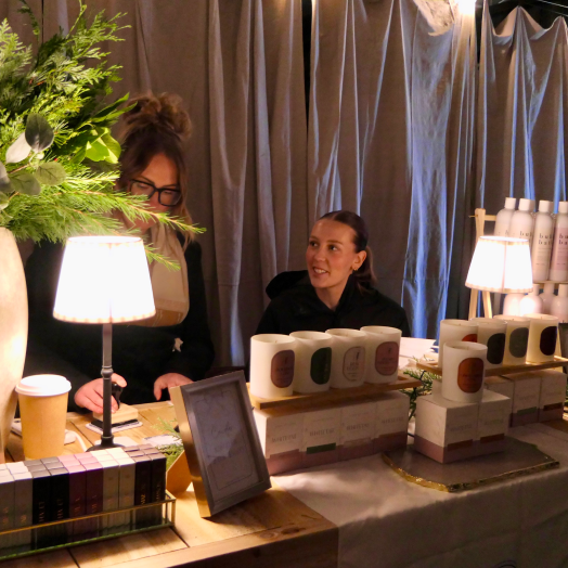 Local artisans at a warmly lit market booth displaying handmade candles and skincare, representing the Artisan Home and Living collection from Farmbox.