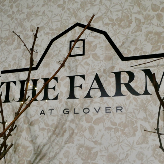 The Farm at Glover logo displayed on a floral patterned wall at a Fraser Valley community event, symbolizing the heart of the Farmbox ecosystem.