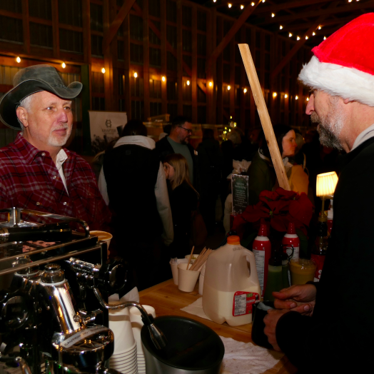 A man in a cowboy hat being served local coffee at a festive Farmbox holiday market in the Fraser Valley, celebrating the connection between growers and neighbours.