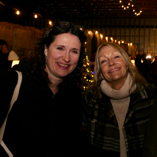 Two women smiling and enjoying a festive community gathering under string lights at The Farm at Glover.